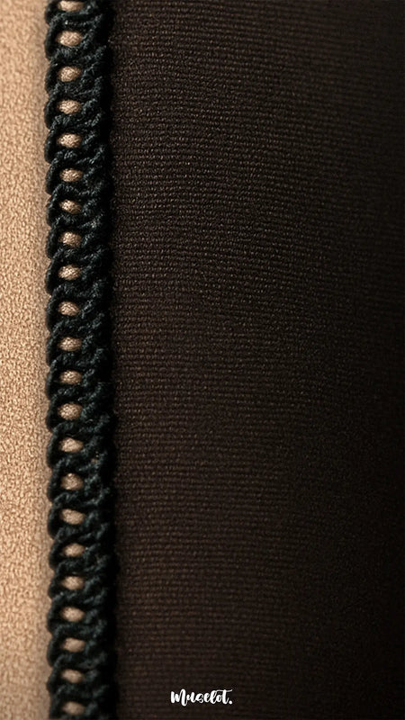 Extreme close-up of the stitching and fabric texture of no-fur sheer effect tights, highlighting the high-quality construction and fine knit. The image showcases the seam where two fabric panels meet—one in nude beige, the other in deep black—joined with a neatly looped black overlock stitch. The fine weave and smooth finish of the material emphasize durability, stretch, and comfort. Captured in a warm studio setting, the image reinforces the craftsmanship behind the product.
