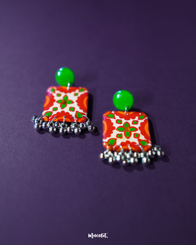 Zarnigar stud earrings rest against a soft purple background, highlighting their vibrant floral motif and charming ghungroo accents. The intricate enamel work and antique finish give these earrings a regal, handcrafted charm that celebrates cultural elegance — Muselot.
