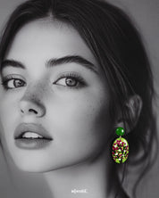 A woman wears the Baaghani handmade drop earrings, highlighting the lively floral design with white and magenta buds on a green base, showcasing the craftsmanship and charm of these statement accessories — Muselot.