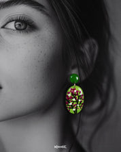 Closeup of a woman wearing the Baaghani handmade drop earrings, highlighting the vivid green base adorned with delicate white and magenta floral motifs, showcasing their vibrant charm and intricate hand-painted details — Muselot.