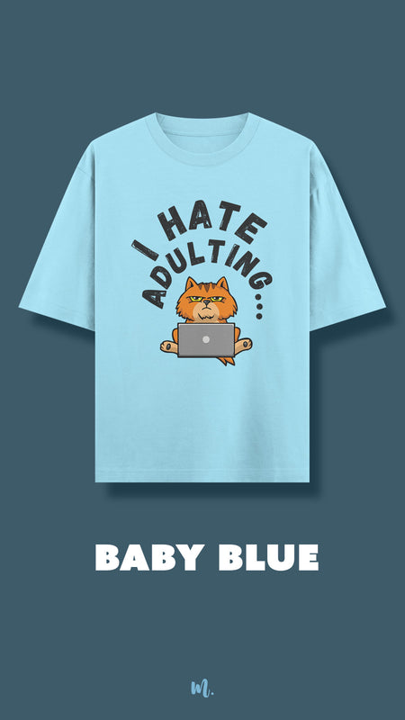 Baby blue oversized t-shirt showcasing a bold “I Hate Adulting” graphic, highlighting the grumpy orange cat illustration with a laptop for a fun, relatable statement design — Muselot.