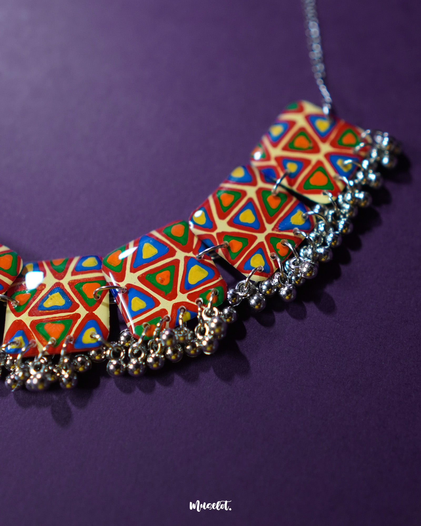 A zoom in shot of a Bandhani handmade necklace, set against a rich purple background, featuring intricate patterns and vibrant colors that highlight its traditional elegance and timeless charm — Muselot.