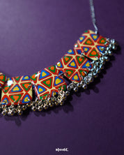 A zoom in shot of a Bandhani handmade necklace, set against a rich purple background, featuring intricate patterns and vibrant colors that highlight its traditional elegance and timeless charm — Muselot.