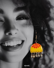 Close-up of a woman wearing the Basantika yellow and red hook earrings, showcasing the vibrant hand-painted pattern and dangling blue beads in intricate detail, highlighting the playful elegance of the design — Muselot.