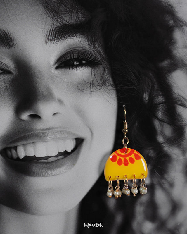 Close-up of a woman wearing the Basantika yellow and red hook earrings, showcasing the vibrant hand-painted pattern and dangling blue beads in intricate detail, highlighting the playful elegance of the design — Muselot.