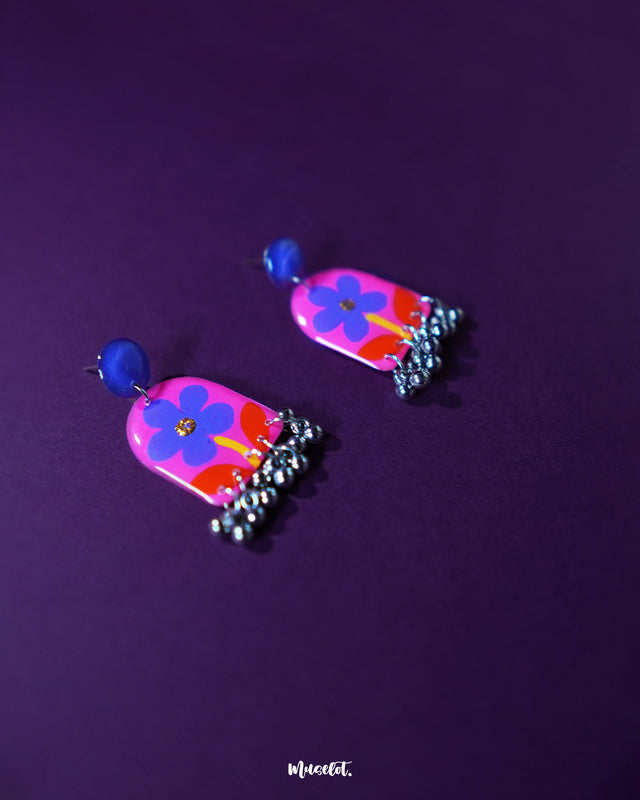 Benazir floral earrings with hand-painted pink and red petals, delicately crafted in a vibrant drop design, set against a rich purple background that highlights their bright, cheerful tones and intricate detailing — Muselot