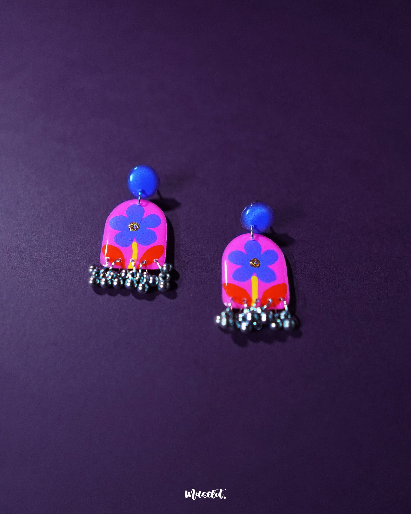 Benazir floral earrings elegantly placed against a soft purple backdrop, featuring intricate purple flowers and bold red leaves that exude a charming, artistic flair — Muselot