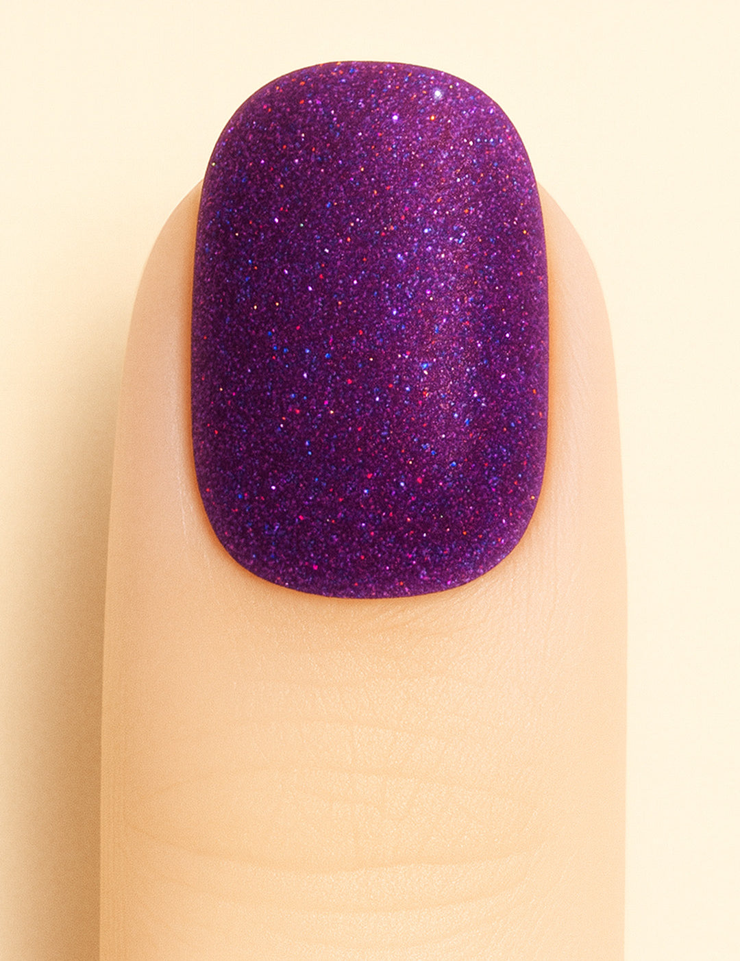 A close-up shot of a model’s finger wearing Berry Cosmos Glitter nail stickies, showcasing a deep purple base filled with fine multicolor glitter specks in pink, blue, and violet. The design highlights the cosmic sparkle and glossy galaxy-like finish that makes this glitter nail art stand out – Muselot.