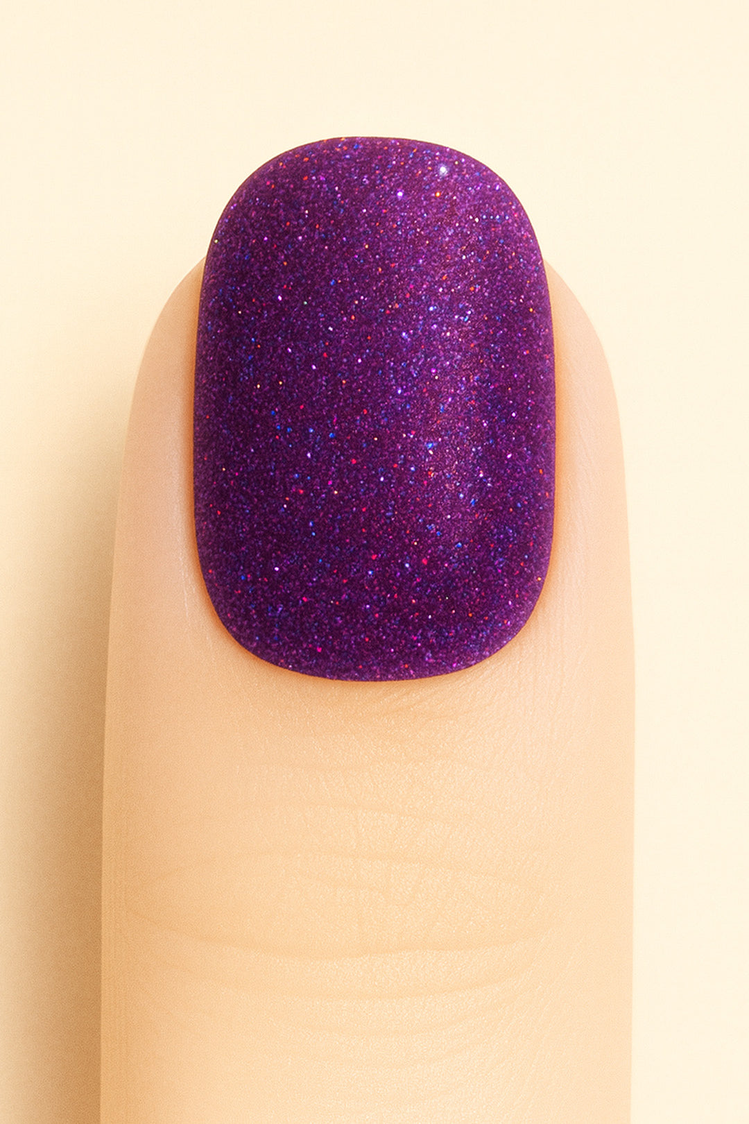 A close-up shot of a model’s finger wearing Berry Cosmos Glitter nail stickies, showcasing a deep purple base filled with fine multicolor glitter specks in pink, blue, and violet. The design highlights the cosmic sparkle and glossy galaxy-like finish that makes this glitter nail art stand out – Muselot.