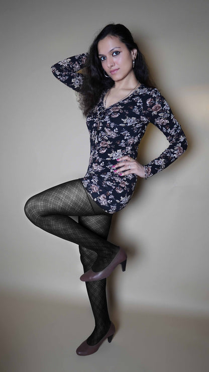 A woman wearing patterned black colored tights for women, posing with her hand on her waist and a leg bent upwards as she stands sideways, looking at the camera, highlighting the stretchable durable material-Muselot