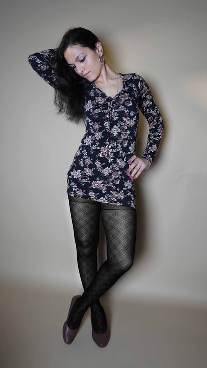 A woman wearing black transparent sheer patterned stockings, posing with her hand on her waist and other behind her head as it is bent sideways, standing cross legged, highlighting the relaxed modern look-Muselot