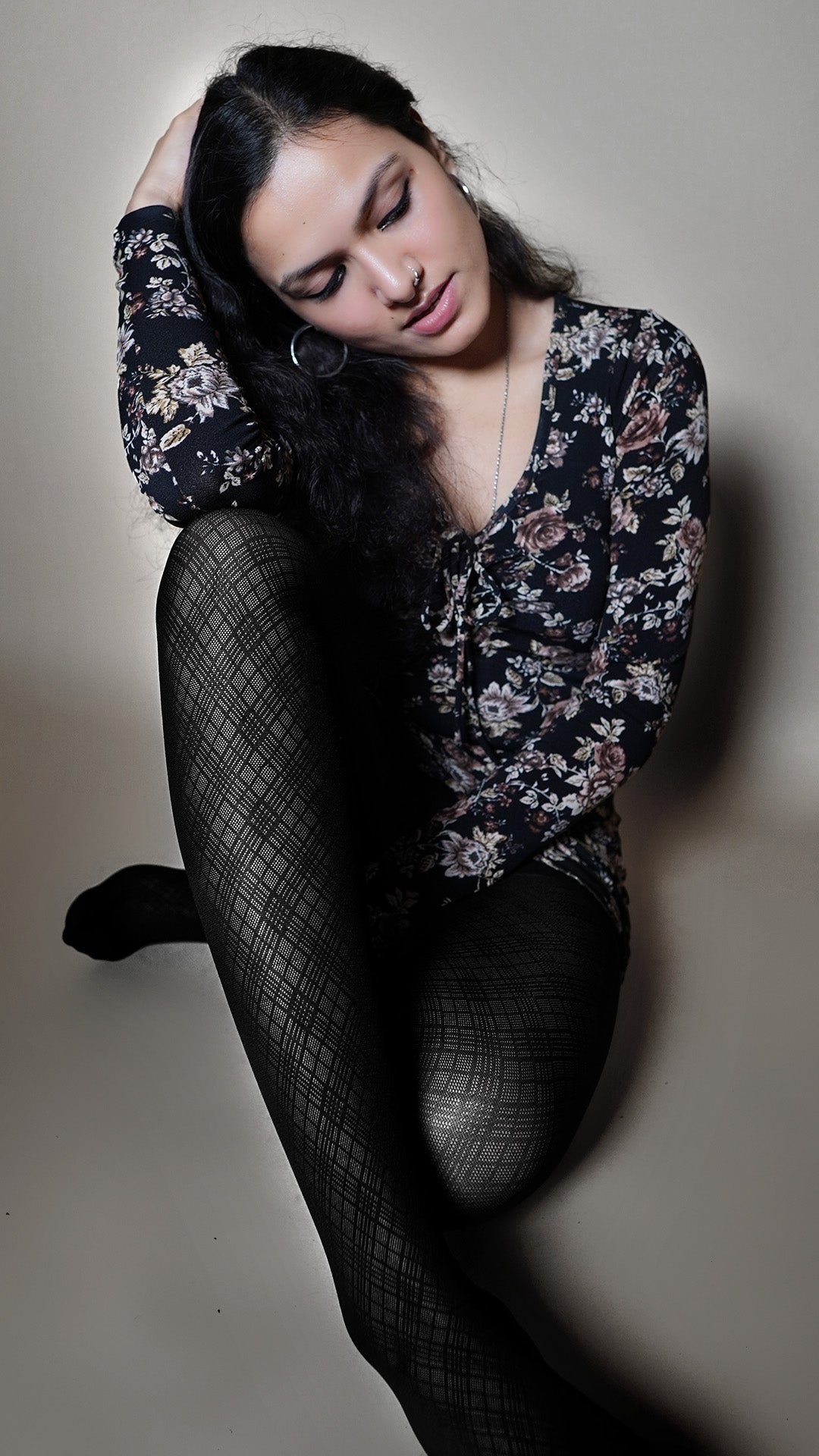 A model wearing the black patterned sheer stockings for girls, sitting with her hand in her hair resting on her knee as she looks sideways with her head bent sideways, highlighting the modern sexy look-Muselot