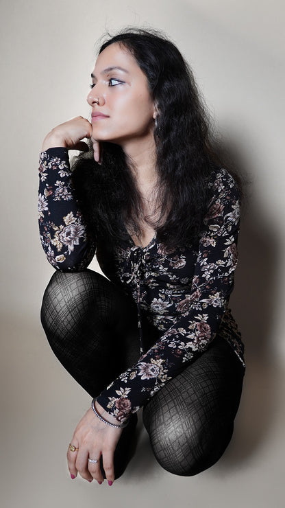 A woman sitting on her feet, her hand beside her chin as she looks sideways, wearing a checkered black transparent moisture wicking nylon tights, showcasing the tear proof stretchable material-Muselot