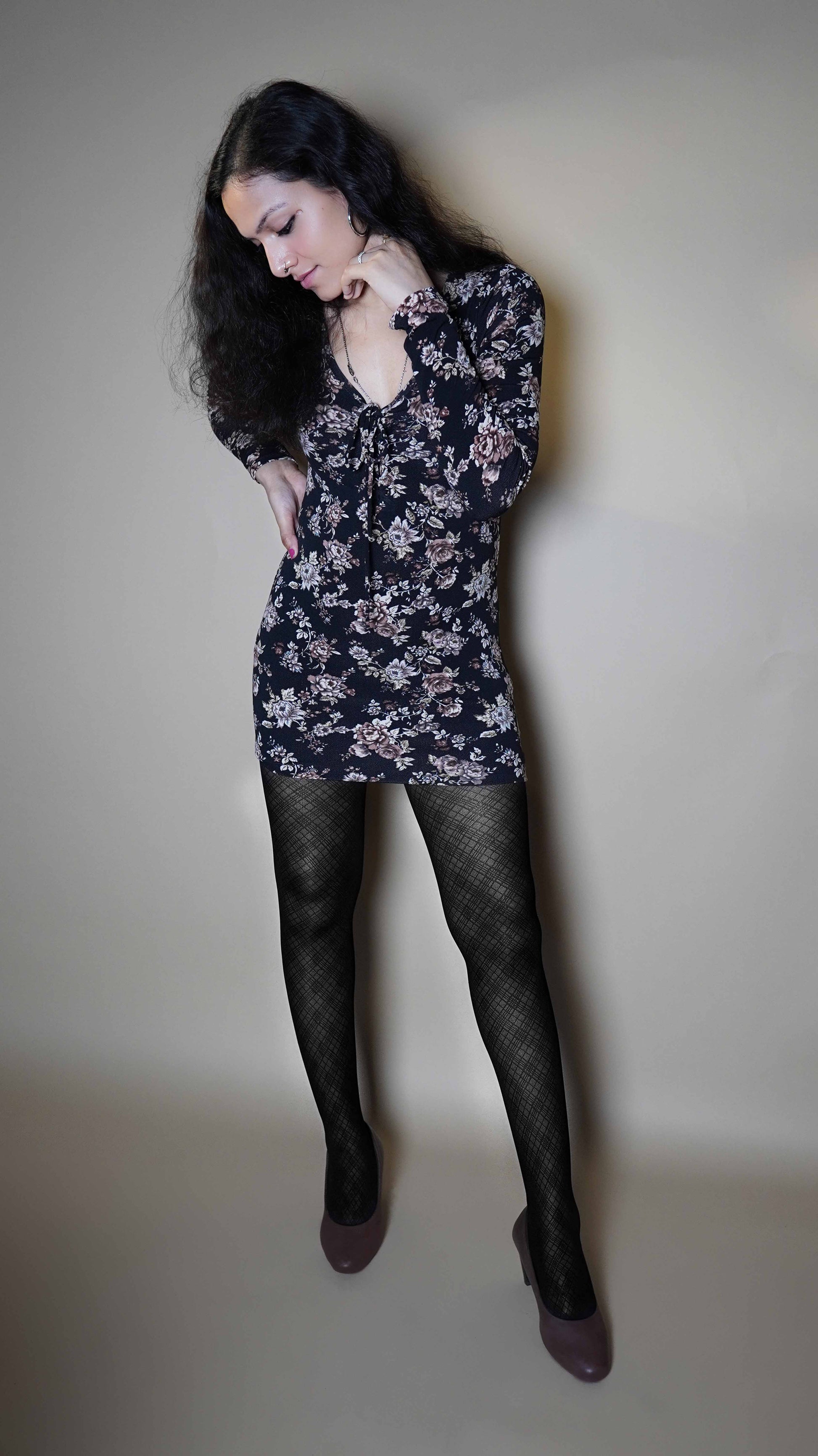 A woman wearing patterned sheer black stocking, posing with her hand on her waist and other gently touching her jawline as she looks downward, highlighting a modish trendy look-Muselot