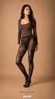 The model wears black rose designer lace stockings on their own, highlighting the sheer floral fishnet pattern, rose motifs and full-length fit – Muselot.