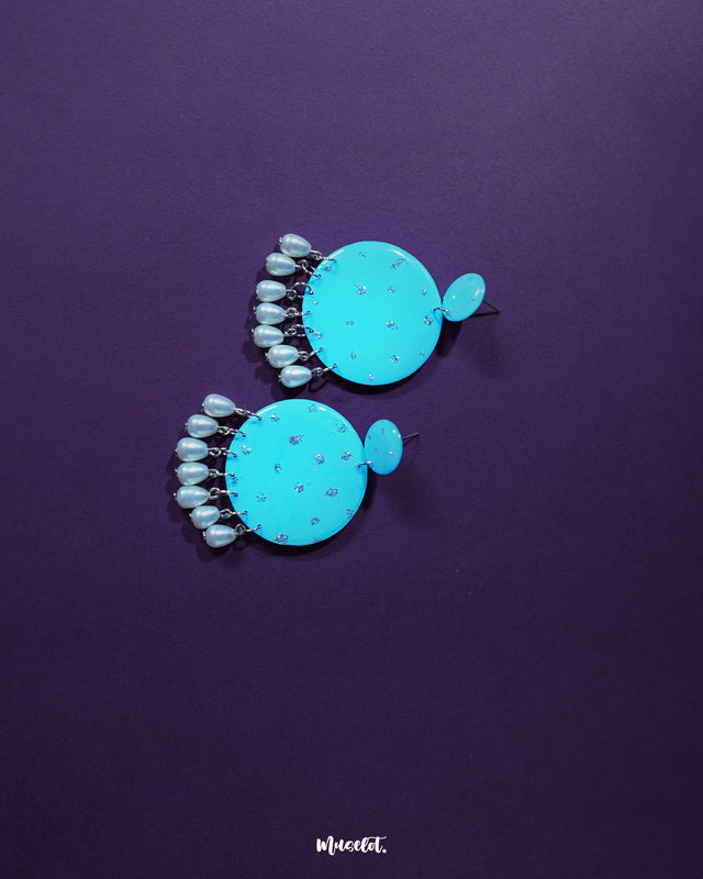 Blue pearl earrings with small and large turquoise blue discs embellished with delicate silver glitter accents, finished with dangling white pearl-like beads, showcased to emphasize their bright color and graceful design – Muselot.