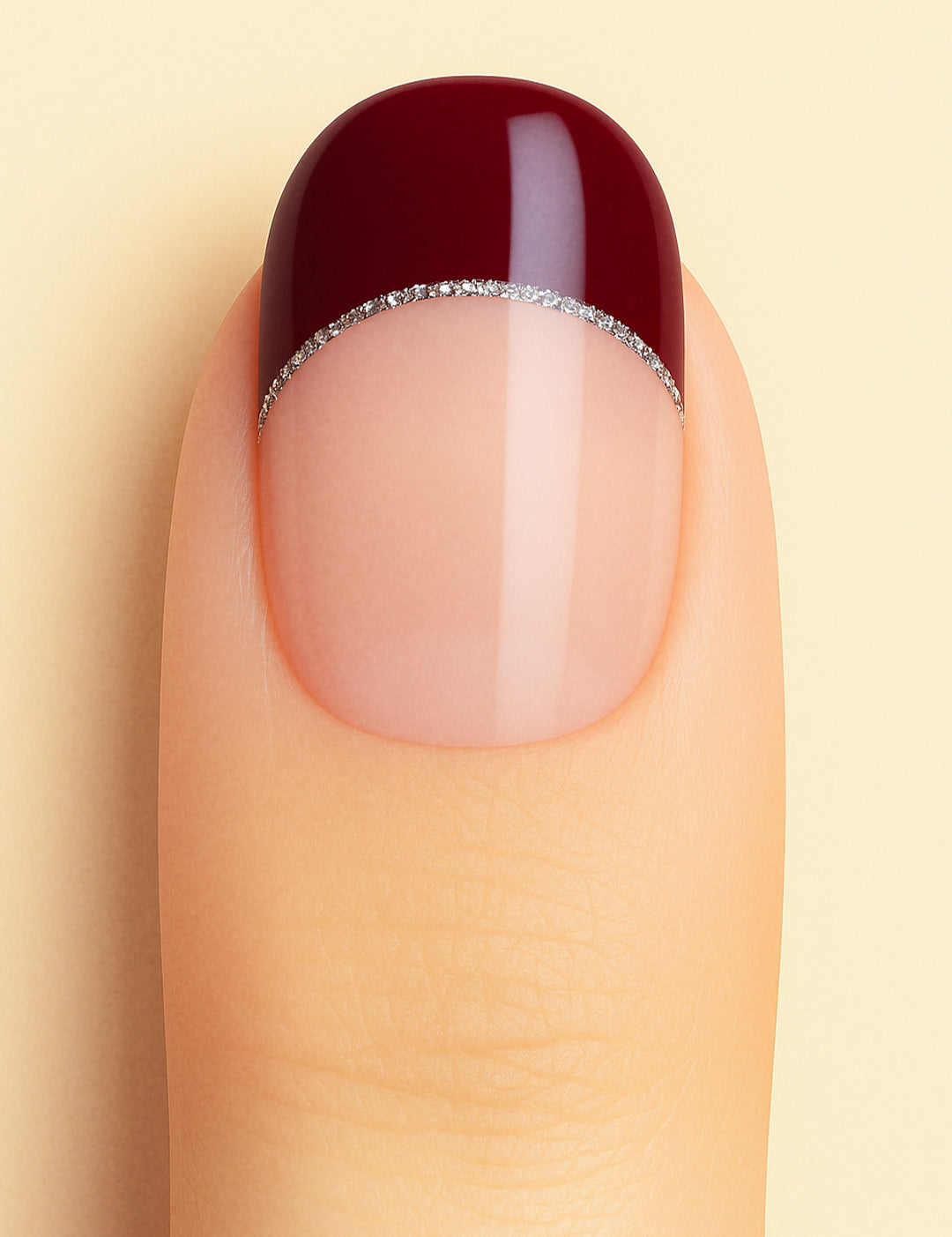 A close-up shot of a model’s finger wearing Cherry Moon French Tip nail stickies, showcasing a deep maroon glossy tip outlined with a fine silver glitter curve over a natural nude base, highlighting a bold and elegant French manicure style with a modern twist – Muselot.