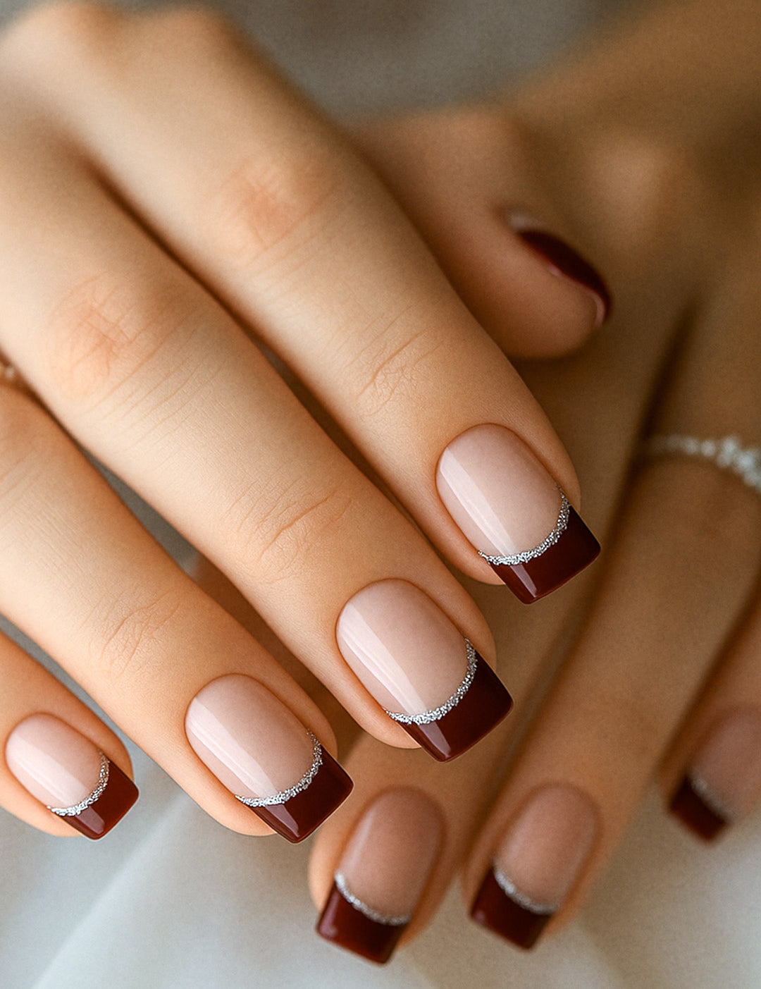 A model’s hand showcasing Cherry Moon French Tip nail stickies, featuring deep maroon glossy tips accented with a fine silver glitter curve over a nude natural base, highlighting the bold yet sophisticated charm of this French manicure design – Muselot.
