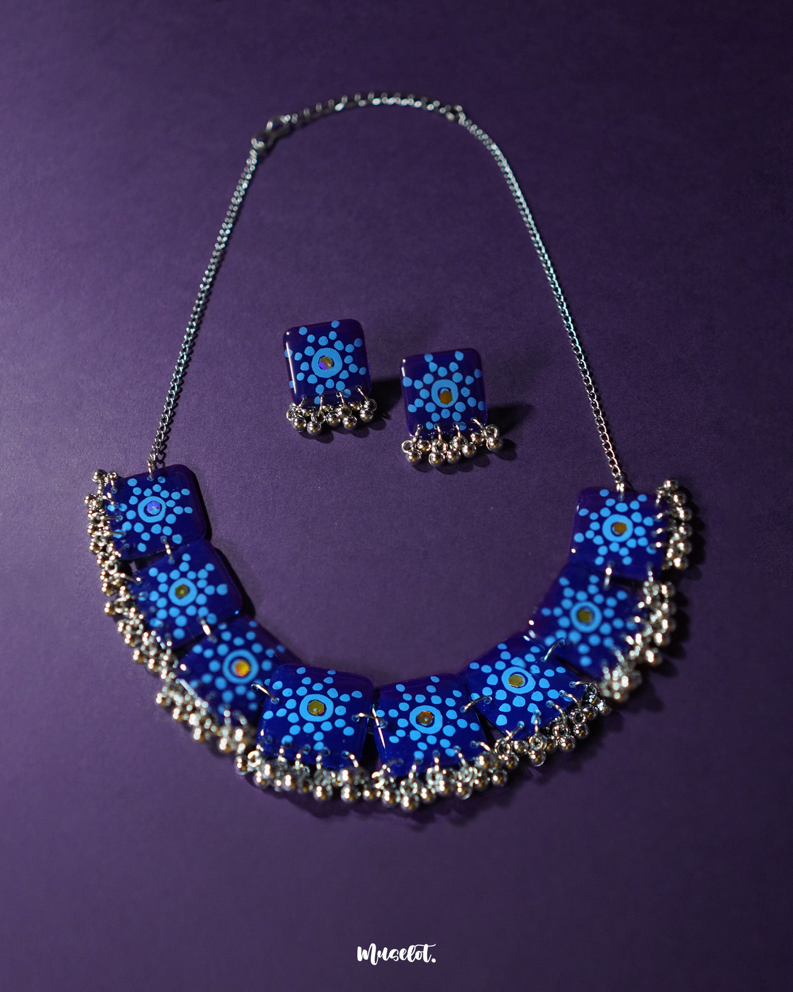 Falakzaar blue necklace and earring set laid out on a purple surface, showcasing the intricate dot mandala pattern on navy blue tiles, accentuated with silver beads for a handcrafted, artistic look — Muselot.