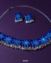 Falakzaar blue necklace and earring set featuring delicate hand-painted floral patterns in white and sky blue on a deep blue base, highlighting the intricate craftsmanship and showcasing graceful ethnic charm — Muselot.