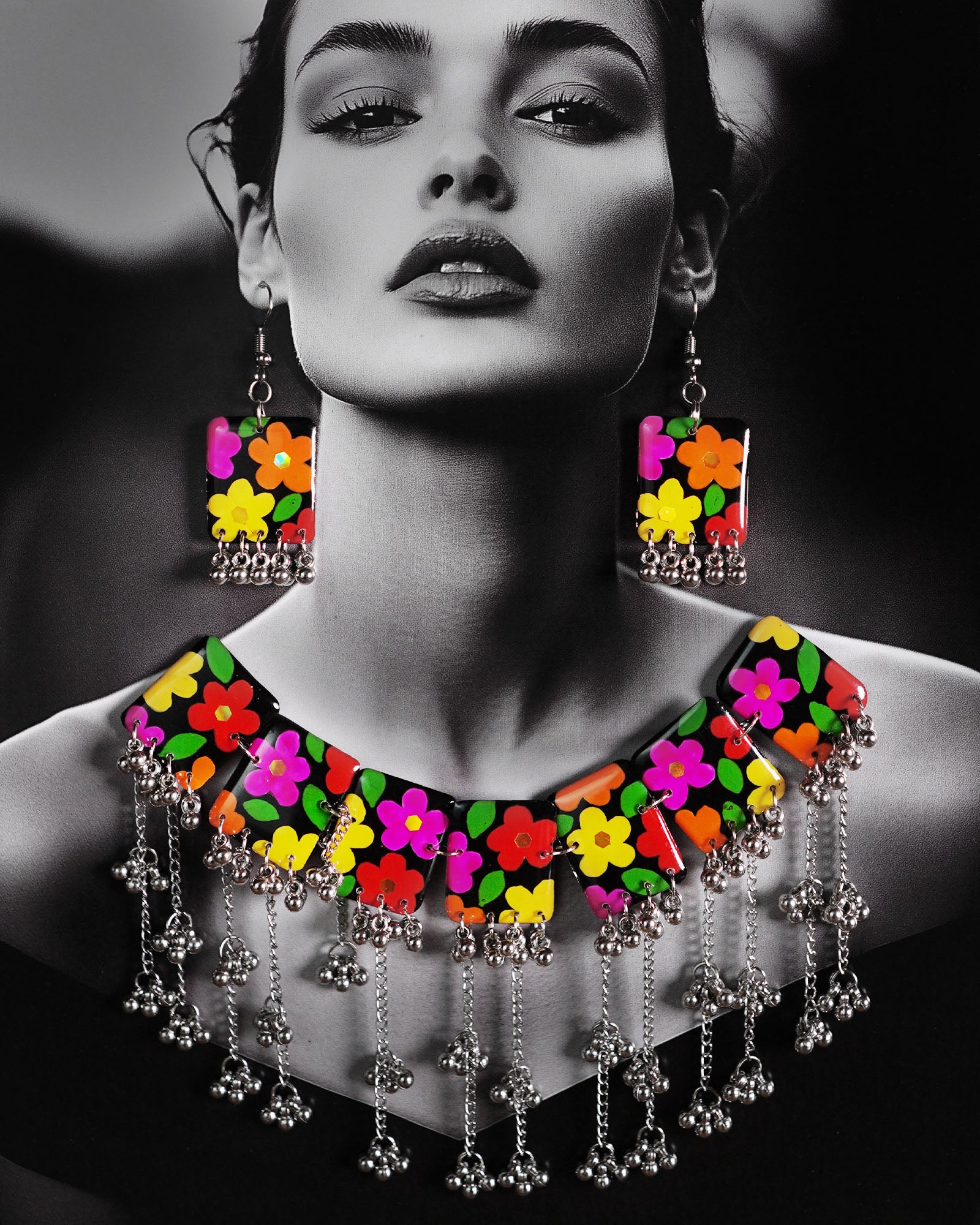 A model wearing the floral jewelry set featuring a bold necklace and matching earrings. The black base is beautifully hand-painted with bright, multicolored flowers, and finished with silver gungroo chains that dangle playfully. The vibrant design stands out against the outfit, adding a joyful, boho charm to the overall look — Muselot.