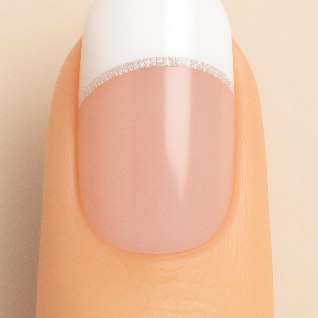 A close-up of a model’s finger featuring Frosted Charm French Tip Nail Stickies by Muselot, designed with a classic white French tip accented by a fine line of subtle glitter, giving a timeless and elegant manicure look with a glossy finish.