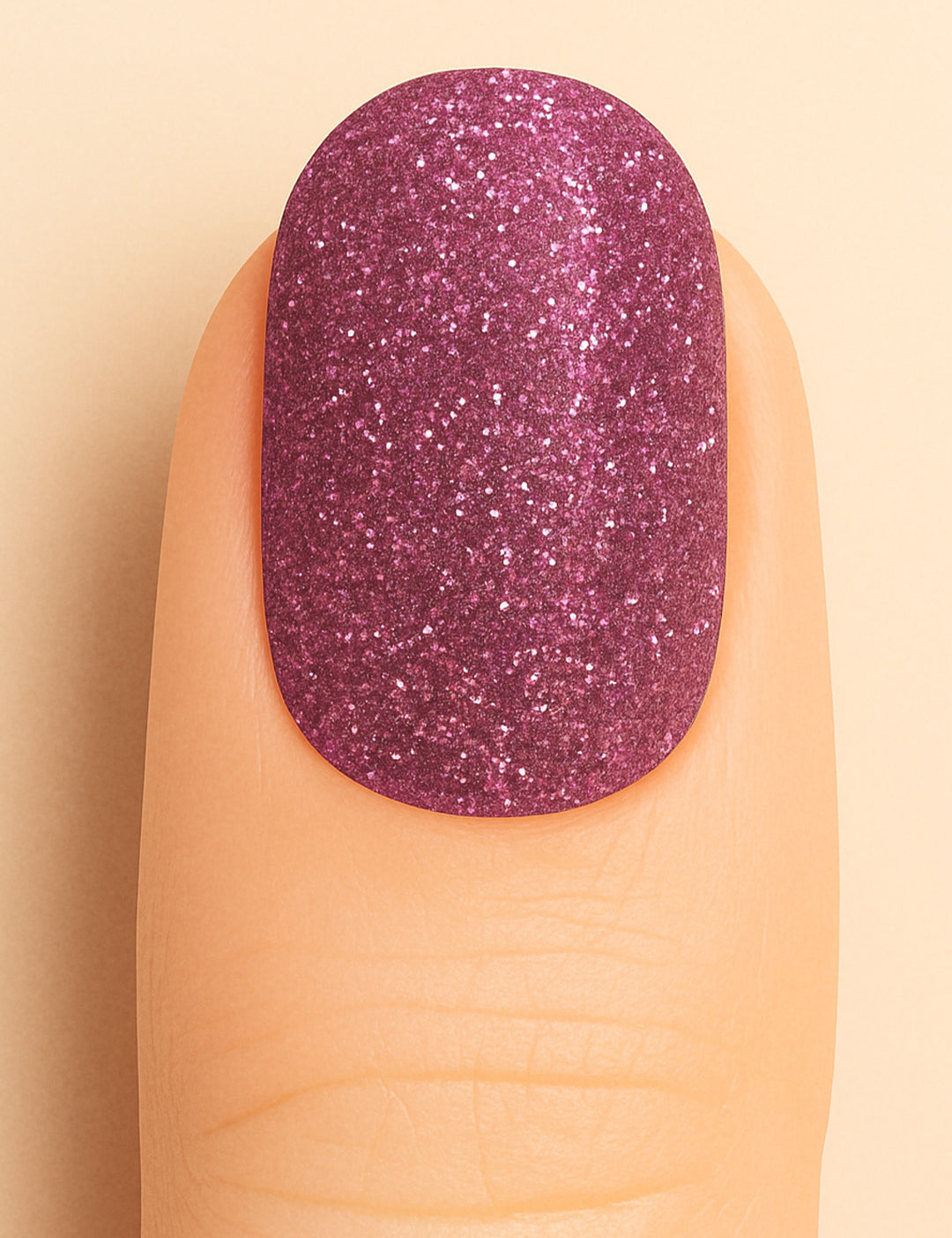 A close-up shot of a finger wearing Glitter Crush nail stickies, showcasing a deep plum-pink shade loaded with fine glitter sparkles, highlighting the rich shimmer and glossy salon-style finish that adds a glamorous pop to the nails – Muselot.