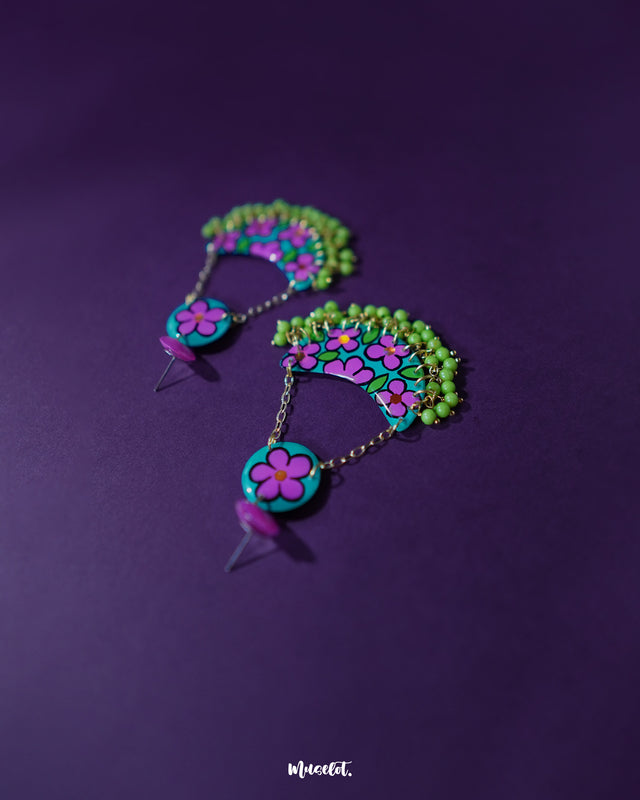 Close-up of Gulbahaar chandbali earrings featuring delicate purple and green floral patterns on a crescent base, with yellow bead accents hanging below, showcasing fine handcrafted detailing — Muselot.
