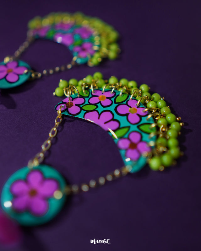A closeup shot of a pair of Gulbahaar chandbali earrings displayed flat against a soft backdrop, showcasing their delicate floral detailing, pearl embellishments, and graceful arc design — Muselot.