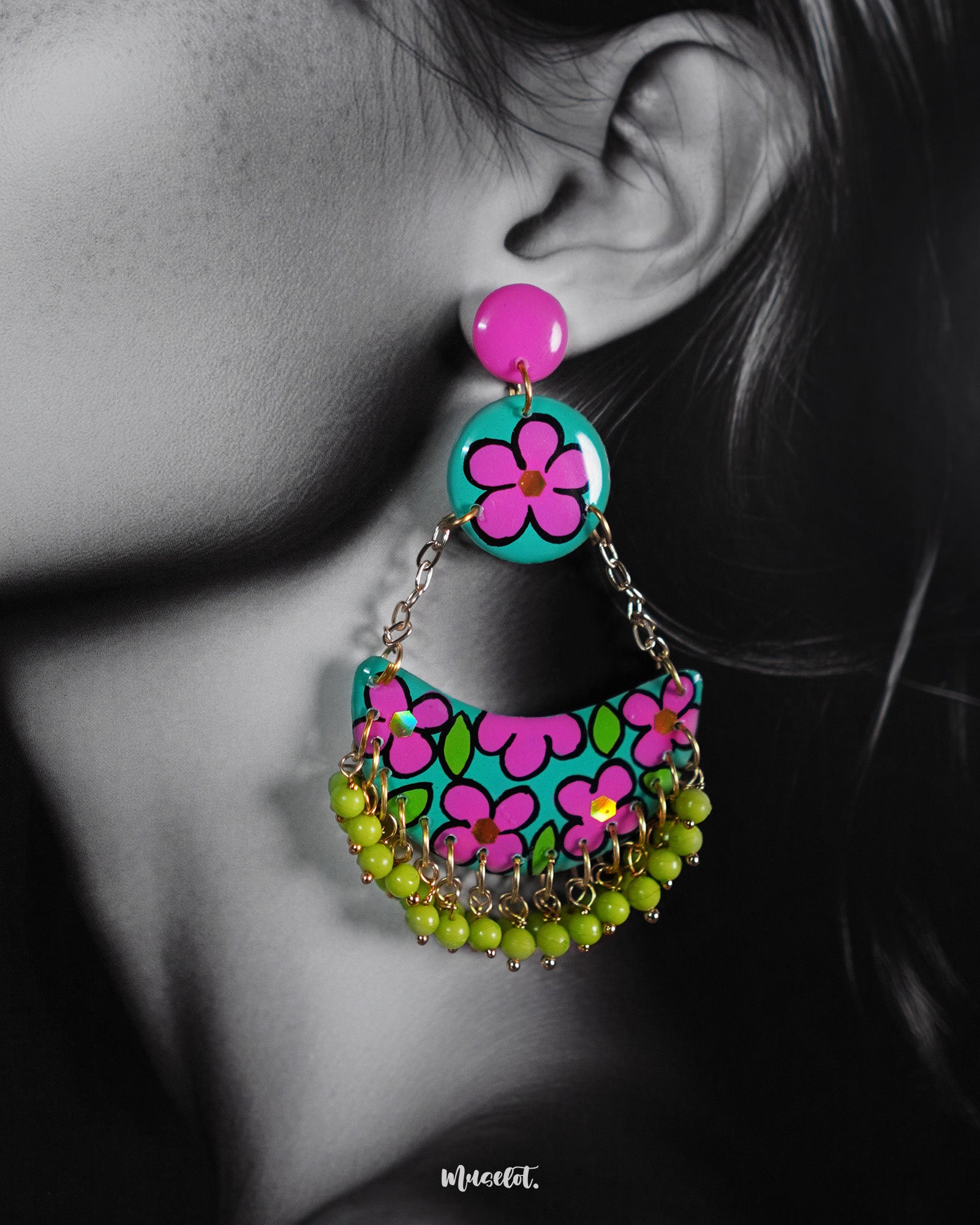 A close-up of a woman wearing Gulbahaar floral earrings, showcasing the vivid teal and magenta hand-painted flowers paired with dangling lime green beads, highlighting their vibrant charm and handmade artistry — Muselot.