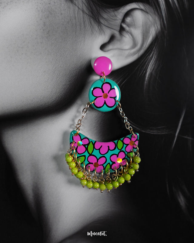 A close-up of a woman wearing Gulbahaar floral earrings, showcasing the vivid teal and magenta hand-painted flowers paired with dangling lime green beads, highlighting their vibrant charm and handmade artistry — Muselot.