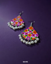 Guldaan floral earrings with hand-painted multicolour blooms and dangling pearl drops, displayed against a purple background to highlight their vibrant folk-inspired design – Muselot.