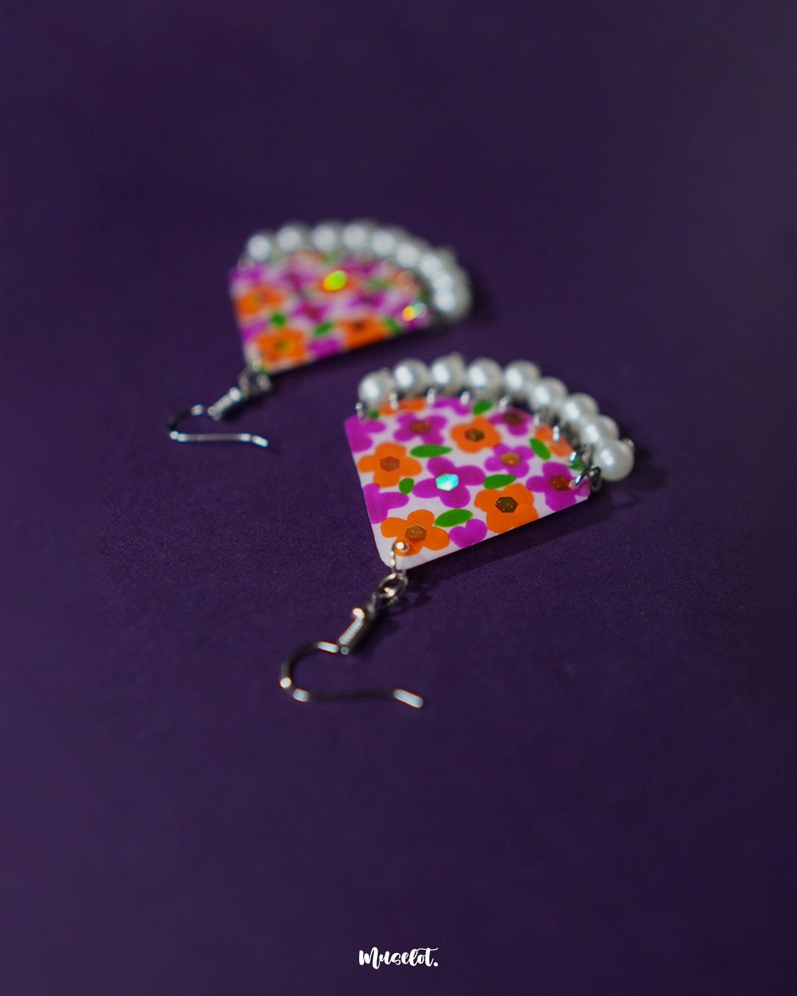 Angled view of Guldaan floral earrings, highlighting the layered hand-painted floral design and dangling pearl drops on a plain background – Muselot.