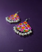 Close-up of Guldaan floral earrings, capturing the vibrant hand-painted flowers and glossy pearl drop detail against a simple backdrop – Muselot.