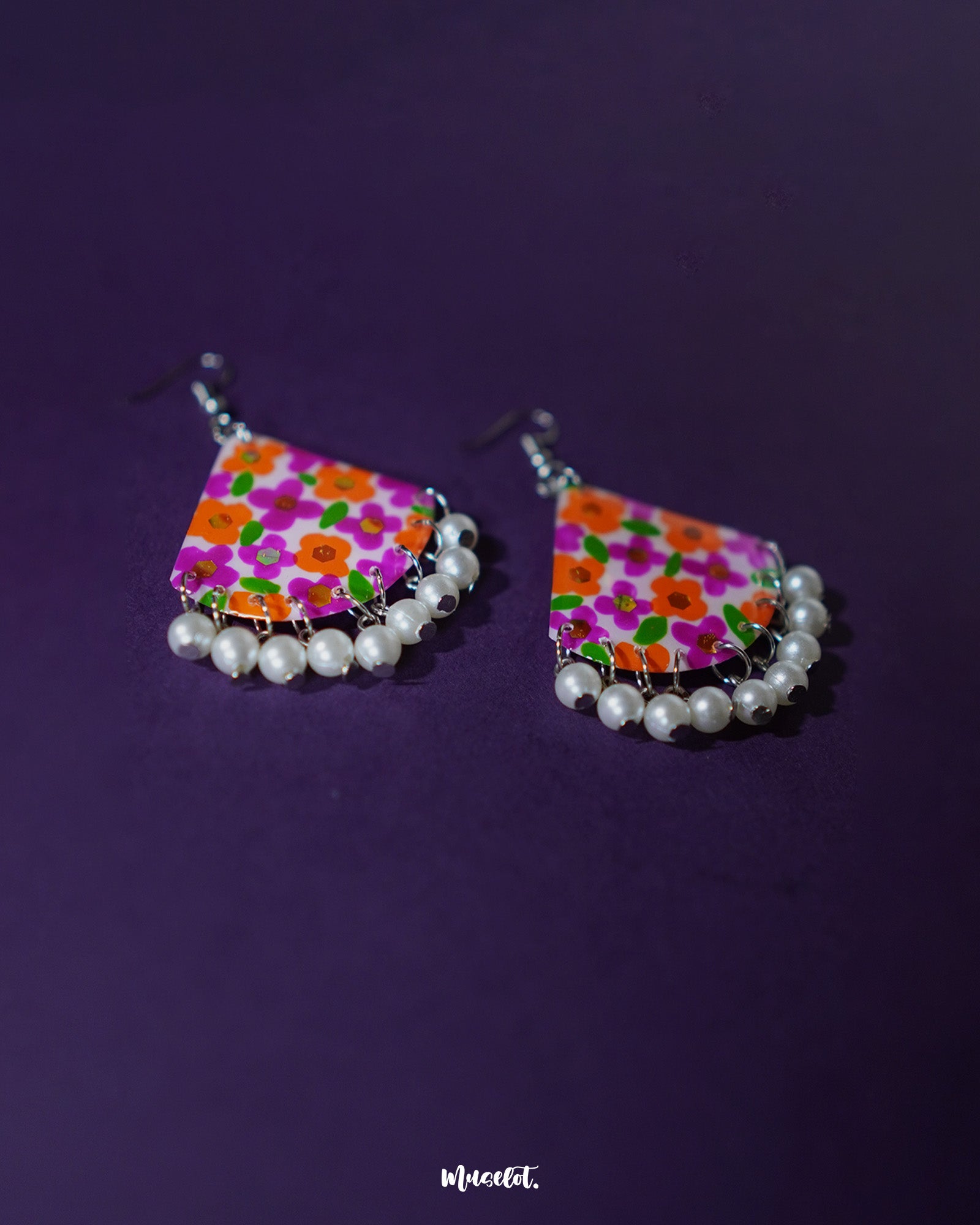 Pair of Guldaan floral earrings laid flat, showcasing multicolour hand-painted blooms and elegant pearl drops on a neutral background – Muselot.
