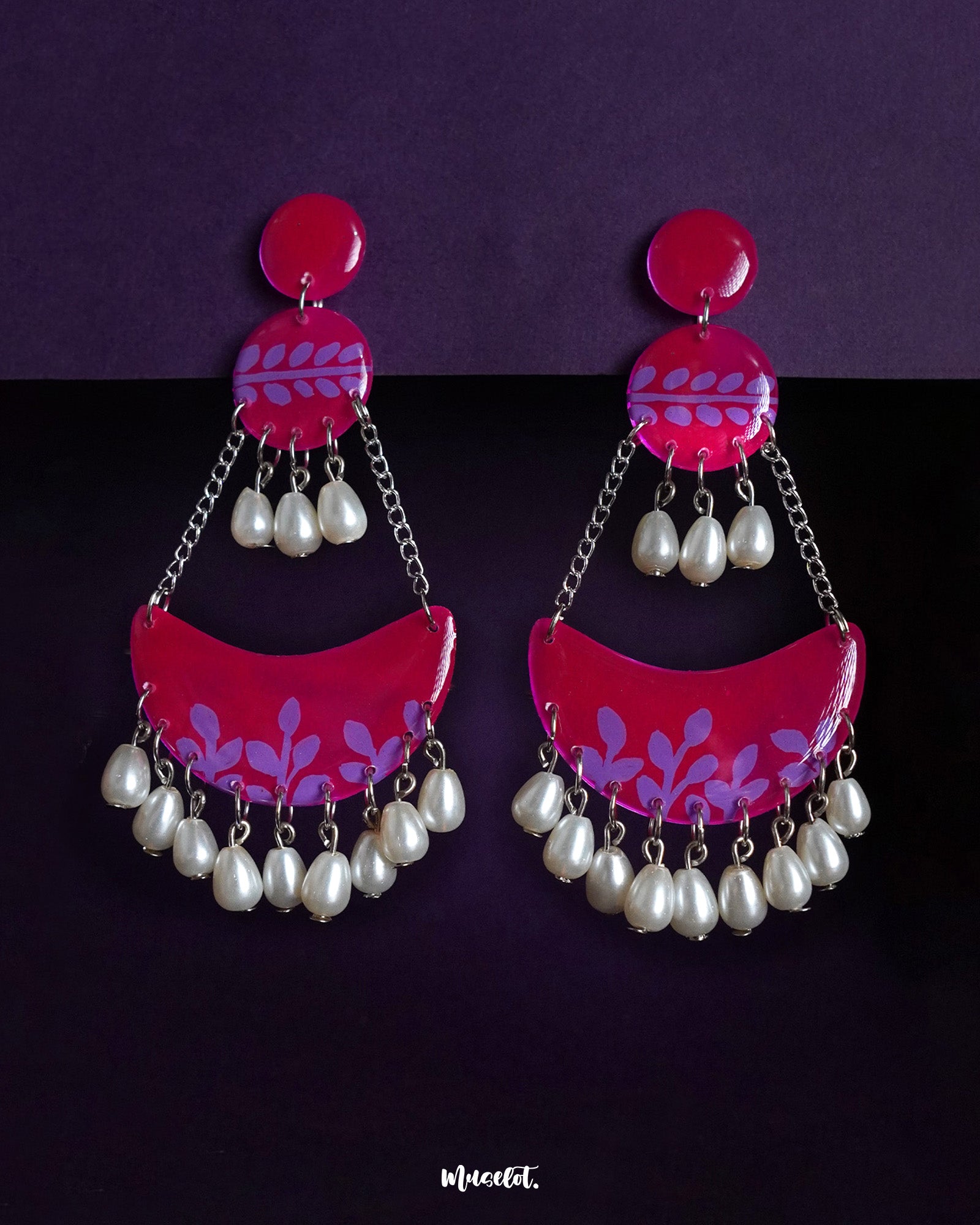 A striking fusion of modern flair and traditional charm, the Gulfaam chandbali earrings feature a hot pink crescent base adorned with purple foliage patterns and cascading pearl drops, creating a look that's both bold and graceful — Muselot.