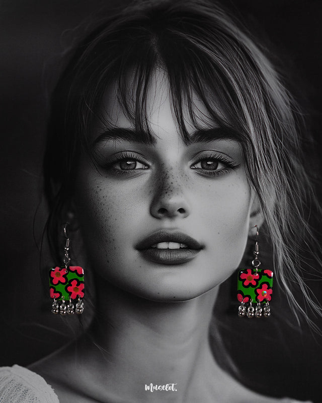 Model wearing the Gulnaar floral earrings, showcasing rectangular charms with bright pink and red flowers on a green background, outlined in black, and accented with delicate silver bead tassels, highlighting their vibrant and playful design – Muselot.