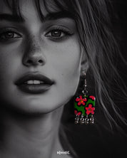 Close-up shot of a model wearing the Gulnaar floral earrings, featuring rectangular charms with vivid pink and red flowers on a green background outlined in black, adorned with delicate silver bead tassels, capturing the bright colors and fine details – Muselot.