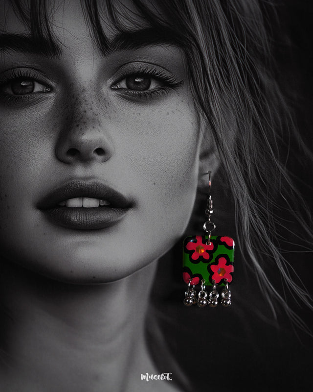 Close-up shot of a model wearing the Gulnaar floral earrings, featuring rectangular charms with vivid pink and red flowers on a green background outlined in black, adorned with delicate silver bead tassels, capturing the bright colors and fine details – Muselot.