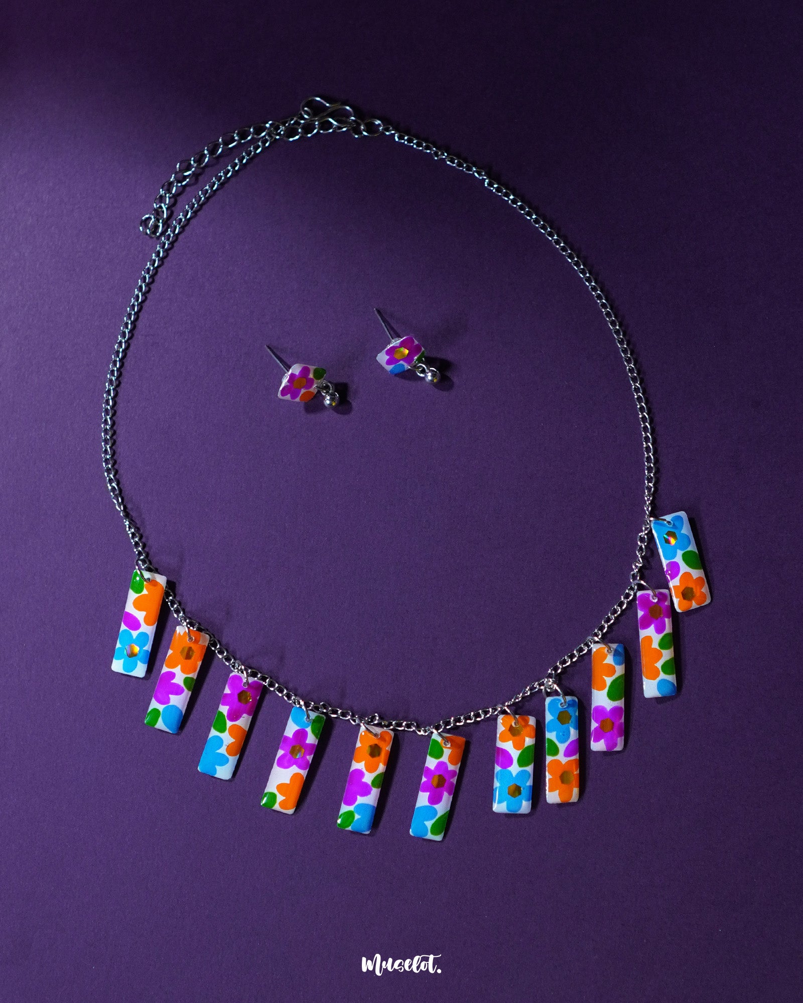 A vibrant close-up of the Gulraas floral necklace set featuring a row of multicolor hand-painted floral charms on a silver-toned chain, paired with matching stud earrings—highlighting its playful charm and boho handcrafted detailing — Muselot