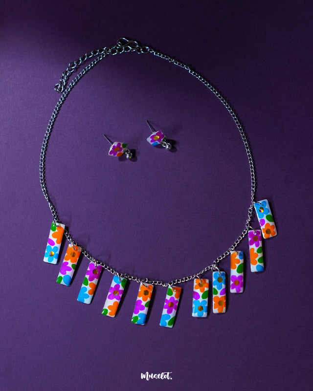 A vibrant close-up of the Gulraas floral necklace set featuring a row of multicolor hand-painted floral charms on a silver-toned chain, paired with matching stud earrings—highlighting its playful charm and boho handcrafted detailing — Muselot