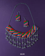 Gulrang multicolor resin jewelry set featuring a silver chain necklace with rectangular charms in bold red, green, blue, and purple diagonal stripes accented with dots, paired with matching earrings and intricate silver bead tassels, beautifully displayed on a deep purple background – Muselot.