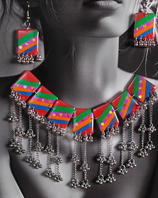 Close-up of model wearing the Gulrang multicolor resin jewelry set, highlighting the bold red, green, blue, and purple striped rectangular charms with dotted accents and cascading silver bead tassels on the necklace, paired with matching earrings, capturing the vibrant details and craftsmanship – Muselot.