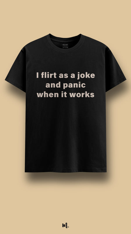 Black graphic t-shirt showcasing the “I flirt as a joke and panic when it works” statement, highlighting a funny, self-aware vibe perfect for casual outings and everyday wear,showcased against a clean beige background – Muselot