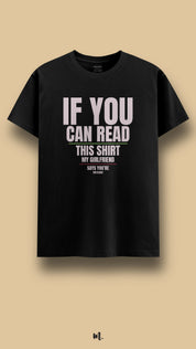 Black graphic t-shirt showcasing the statement “IF YOU CAN READ THIS SHIRT MY GIRLFRIEND SAYS YOU’RE TOO CLOSE!” in large high-contrast lettering with subtle color accents, highlighting funny possessive relationship humor against a clean beige studio backdrop – Muselot