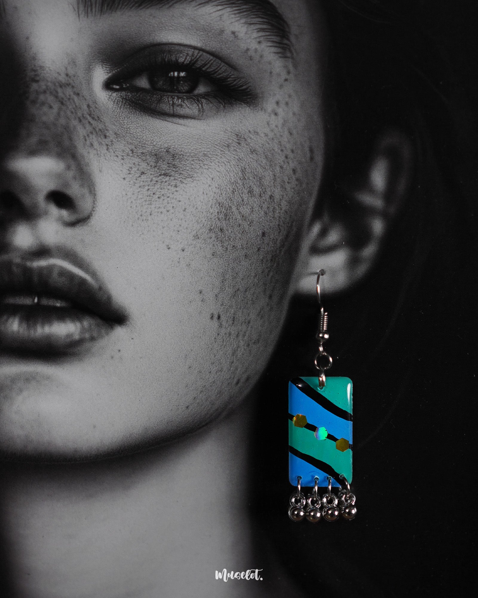 A woman wearing the Jaltarang boho drop earrings shows off their intricate hand-painted aqua detailing and dangling silver elements, capturing a free-spirited, earthy elegance—Muselot.