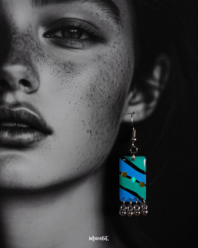 A woman wearing the Jaltarang boho drop earrings shows off their intricate hand-painted aqua detailing and dangling silver elements, capturing a free-spirited, earthy elegance—Muselot.