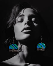A woman wears the Jaltarang drop earrings, showcasing their vibrant turquoise and blue hand-painted design with yellow dot accents and silver ghungroo danglers that add movement and charm—Muselot.