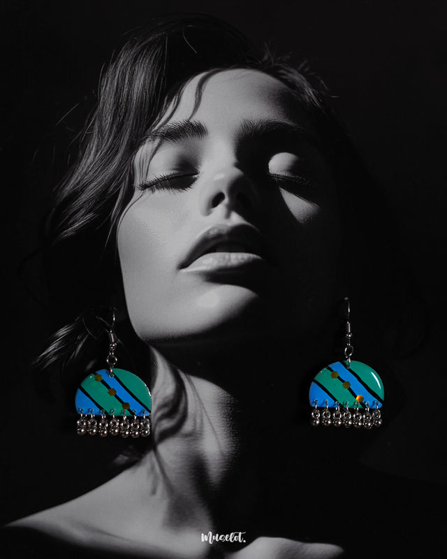 A woman wears the Jaltarang drop earrings, showcasing their vibrant turquoise and blue hand-painted design with yellow dot accents and silver ghungroo danglers that add movement and charm—Muselot.