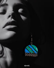 Close-up of a woman wearing the Jaltarang drop earrings, highlighting the bold blue and green diagonal stripes, yellow dot detailing, and delicate silver ghungroo accents that create a rhythmic, eye-catching appeal—Muselot